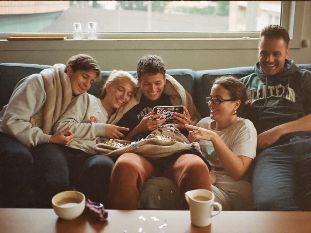 Fünf Freunde sitzen am Morgen danach auf dem Sofa und schauen sich gemeinsam die Fotos der Nacht an